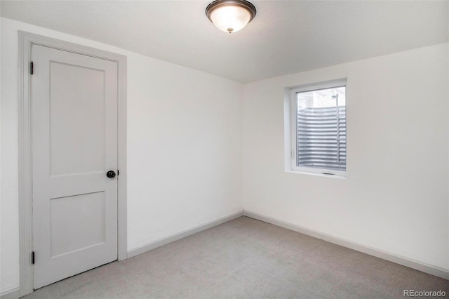 spare room with baseboards and light carpet