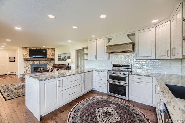 6451 Crestbrook Dr, Morrison, CO 80465 - kitchen featuring range with two ovens, custom range hood, a peninsula, a fireplace, and dark wood-style floors