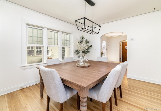 dining area with light wood-type flooring, crown molding, and a notable chandelier