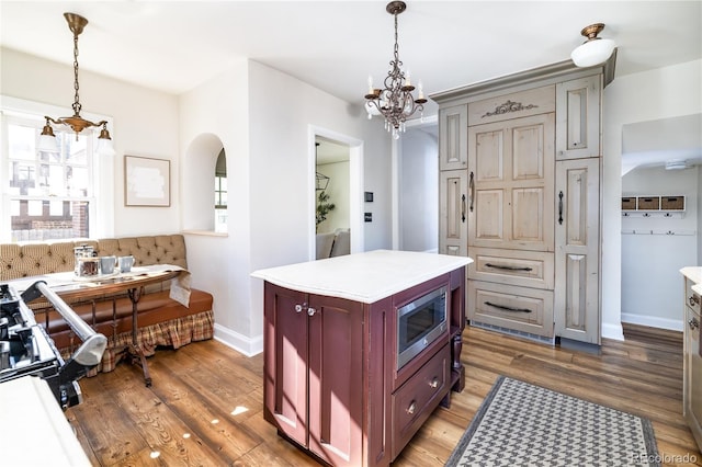 kitchen with pendant lighting, a center island, stainless steel microwave, and light wood-type flooring