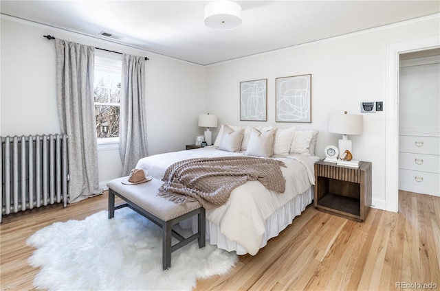 bedroom featuring light wood-type flooring, radiator heating unit, and ornamental molding