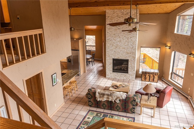 tiled living room featuring wood ceiling, a large fireplace, ceiling fan, and a high ceiling