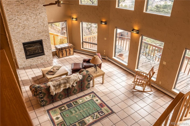 living room with a high ceiling, light tile patterned flooring, a large fireplace, and ceiling fan