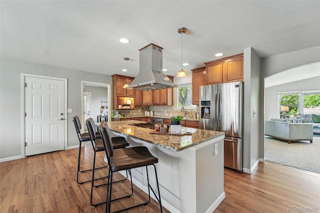 3570 E Arapahoe Pl, Centennial, CO 80122 - kitchen featuring stainless steel fridge, island exhaust hood, brown cabinetry, baseboards, and light stone countertops