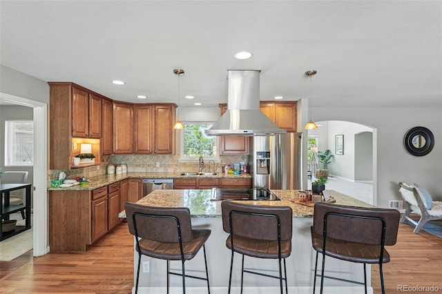 3570 E Arapahoe Pl, Centennial, CO 80122 - kitchen featuring island range hood, stainless steel appliances, brown cabinets, arched walkways, and light wood-type flooring