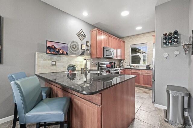 kitchen with backsplash, a sink, a peninsula, dark stone counters, and stainless steel appliances