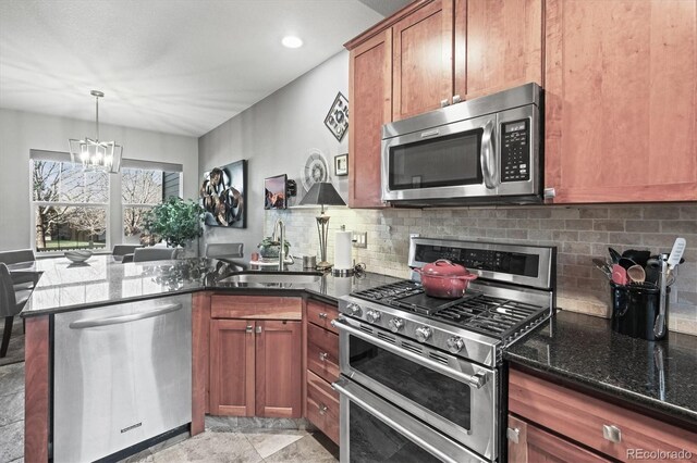 kitchen with appliances with stainless steel finishes, an inviting chandelier, a sink, dark stone counters, and a peninsula