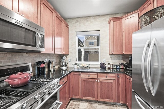 kitchen featuring brown cabinets, stainless steel appliances, dark stone countertops, and tasteful backsplash