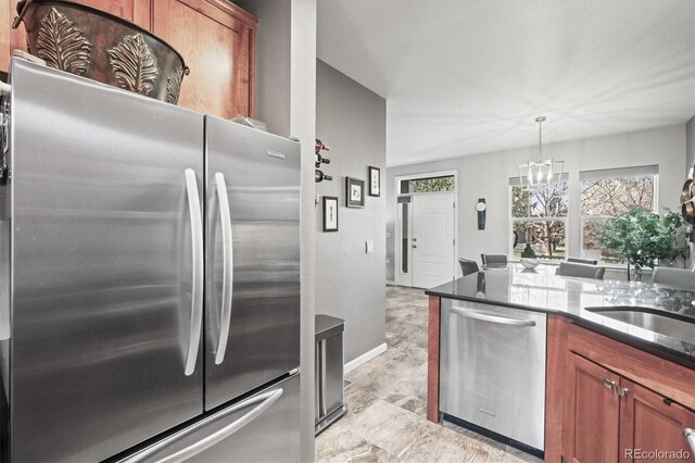 kitchen with brown cabinetry, baseboards, a notable chandelier, dark stone counters, and stainless steel appliances