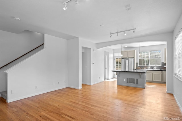 701 N Roslyn St Unit 36, Denver, CO 80230 - unfurnished living room featuring rail lighting, arched walkways, light wood-style flooring, and stairway