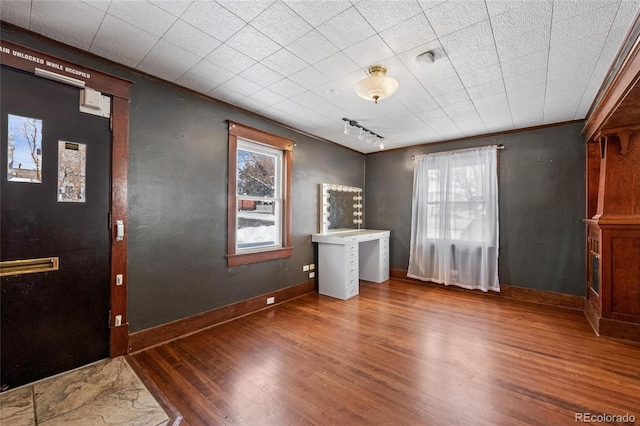 unfurnished room with track lighting, baseboards, dark wood-type flooring, and crown molding