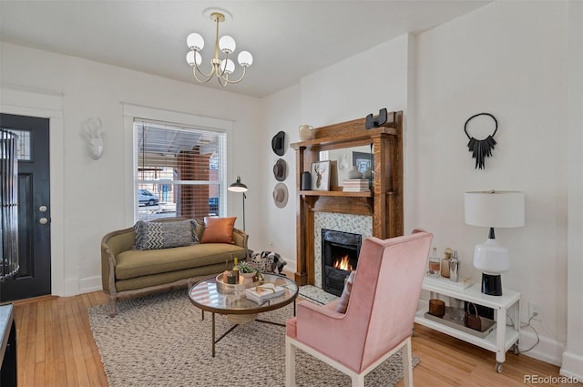 living area featuring a chandelier, light wood finished floors, a fireplace, and baseboards