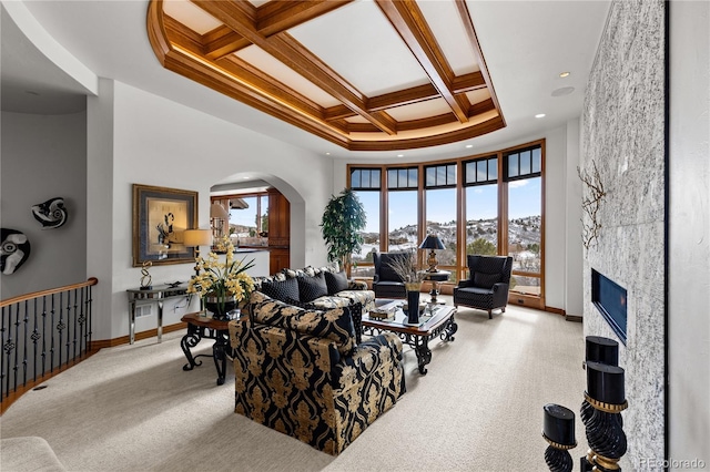 carpeted living room with beamed ceiling, crown molding, coffered ceiling, a high ceiling, and a tiled fireplace