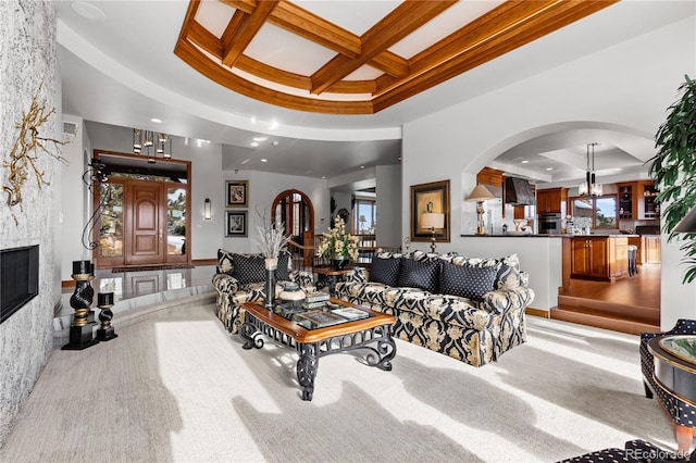 carpeted living room featuring crown molding, beam ceiling, a tray ceiling, a notable chandelier, and coffered ceiling