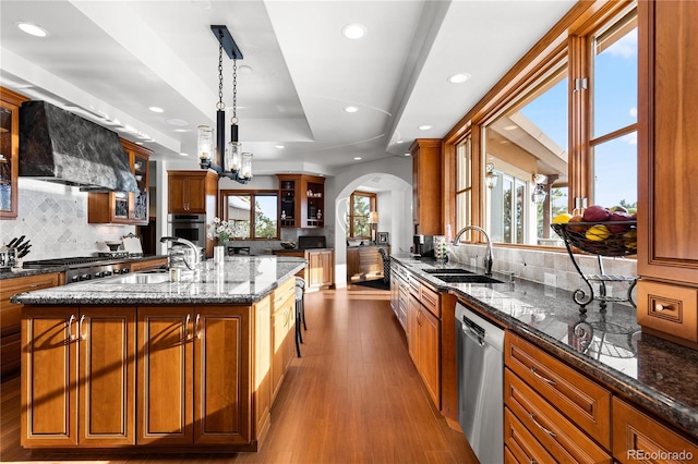 kitchen featuring dark stone counters, hanging light fixtures, sink, stainless steel appliances, and a center island with sink