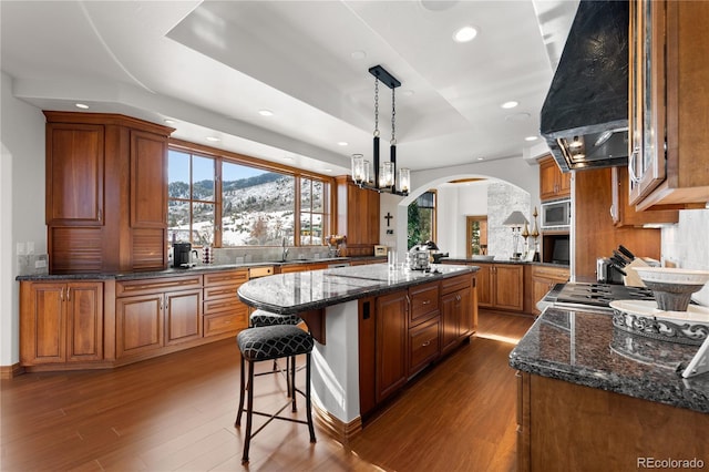 kitchen featuring stainless steel microwave, hanging light fixtures, a mountain view, a center island, and island range hood