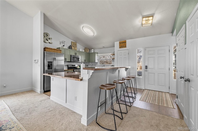 kitchen with green cabinets, a breakfast bar, lofted ceiling, light carpet, and stainless steel appliances