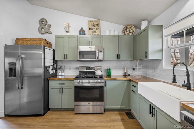 kitchen featuring wood counters, appliances with stainless steel finishes, green cabinets, and light wood-style floors