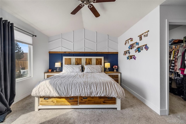 carpeted bedroom featuring a walk in closet, a closet, baseboards, ceiling fan, and vaulted ceiling