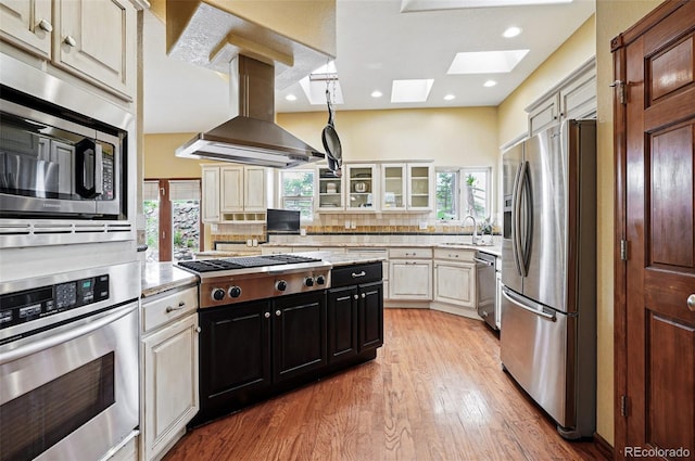 19640 Four Winds Way, Monument, CO 80132 - kitchen with appliances with stainless steel finishes, a skylight, island exhaust hood, light wood finished floors, and glass insert cabinets