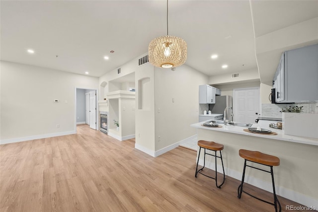 9590 E Florida Ave Unit 1025, Denver, CO 80247 - kitchen with a peninsula, light wood-style flooring, a kitchen bar, tasteful backsplash, and light countertops
