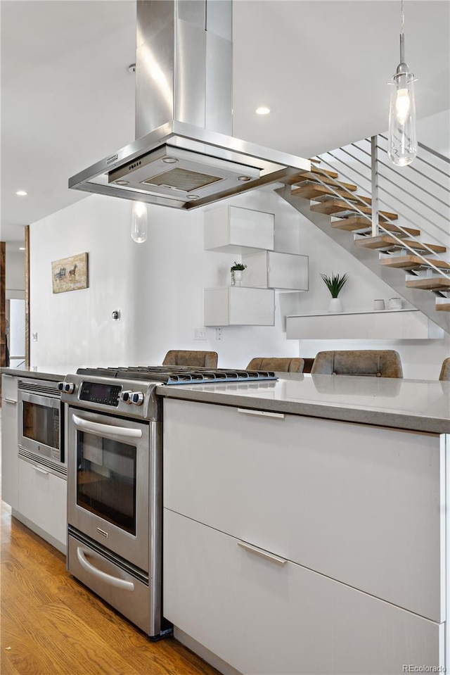 1930 W 35th Ave, Denver, CO 80211 - kitchen with island exhaust hood, stainless steel appliances, white cabinetry, light wood-style floors, and recessed lighting