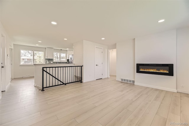 unfurnished living room with visible vents, light wood-type flooring, recessed lighting, and a glass covered fireplace