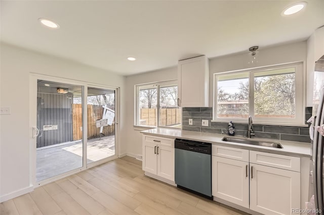 kitchen with white cabinets, a sink, light countertops, stainless steel dishwasher, and decorative backsplash