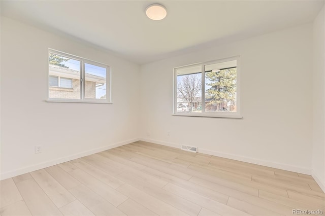 unfurnished room featuring visible vents, baseboards, light wood finished floors, and plenty of natural light