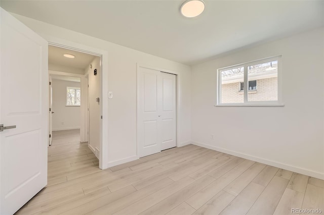 unfurnished bedroom with light wood-style flooring, a closet, and baseboards