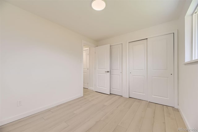 unfurnished bedroom with light wood finished floors, baseboards, and two closets