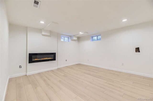 below grade area featuring a glass covered fireplace, baseboards, recessed lighting, light wood-style flooring, and visible vents