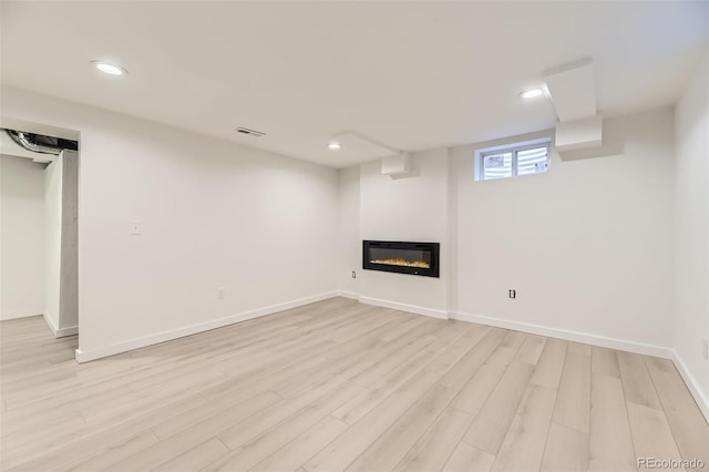 basement with light wood finished floors, a glass covered fireplace, visible vents, and recessed lighting