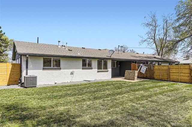 back of house with roof with shingles, a yard, a fenced backyard, and brick siding