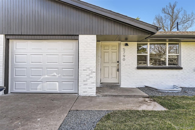 view of exterior entry with brick siding, a garage, and concrete driveway