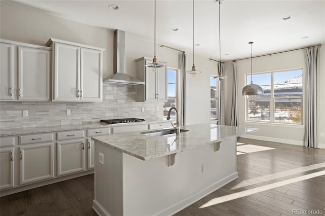 kitchen with backsplash, a center island with sink, wall chimney range hood, sink, and decorative light fixtures