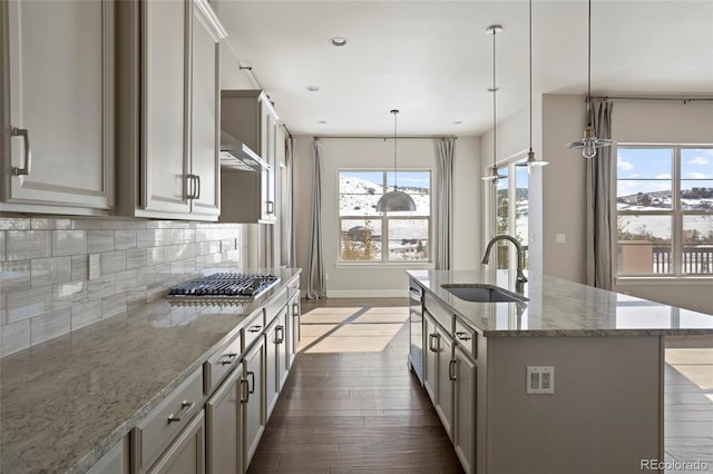 kitchen with dark hardwood / wood-style flooring, light stone counters, sink, pendant lighting, and a center island with sink