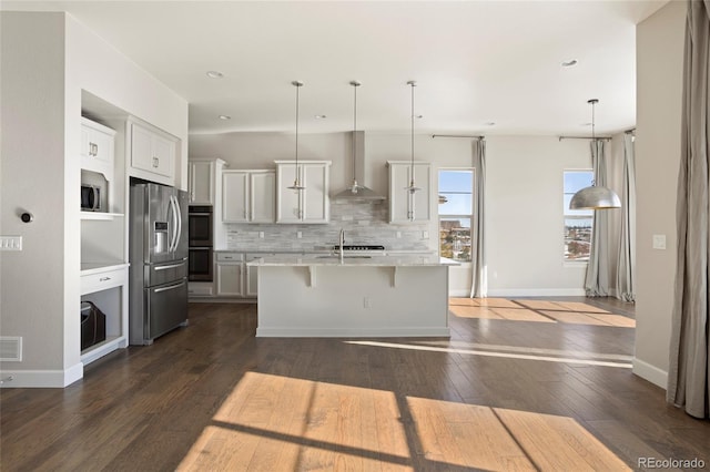 kitchen featuring stainless steel fridge with ice dispenser, hanging light fixtures, a center island with sink, and wall chimney range hood