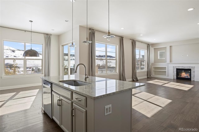 kitchen with hanging light fixtures, sink, a kitchen island with sink, and light stone counters