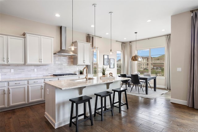 kitchen featuring wall chimney exhaust hood, a sink, gas cooktop, white cabinetry, and tasteful backsplash