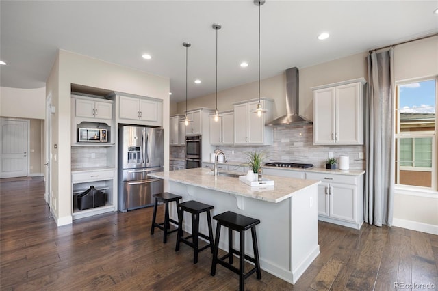 kitchen with wall chimney range hood, appliances with stainless steel finishes, a sink, decorative backsplash, and a kitchen breakfast bar
