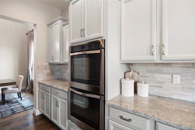 kitchen with stainless steel double oven, decorative backsplash, light stone countertops, dark wood-style flooring, and baseboards