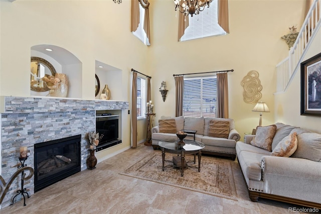 living room with a stone fireplace, a high ceiling, and a chandelier