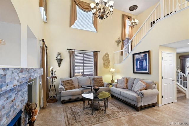 living area with a stone fireplace, stairway, an inviting chandelier, and a towering ceiling