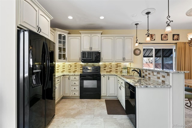 kitchen featuring light stone counters, decorative backsplash, a peninsula, black appliances, and a sink