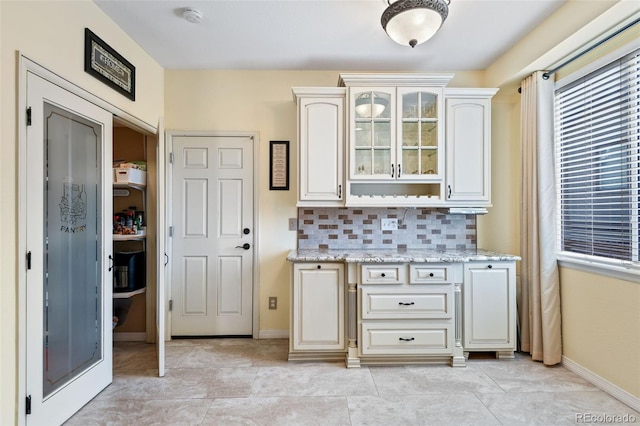 kitchen with backsplash, glass insert cabinets, baseboards, and light stone countertops