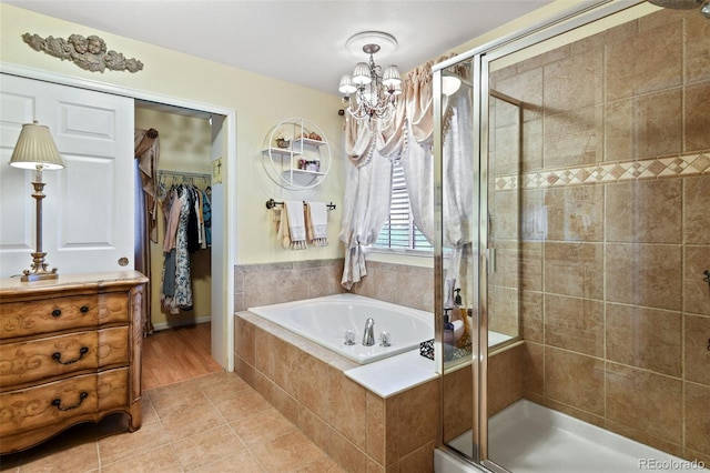 full bath featuring a spacious closet, a shower stall, a garden tub, tile patterned floors, and a notable chandelier