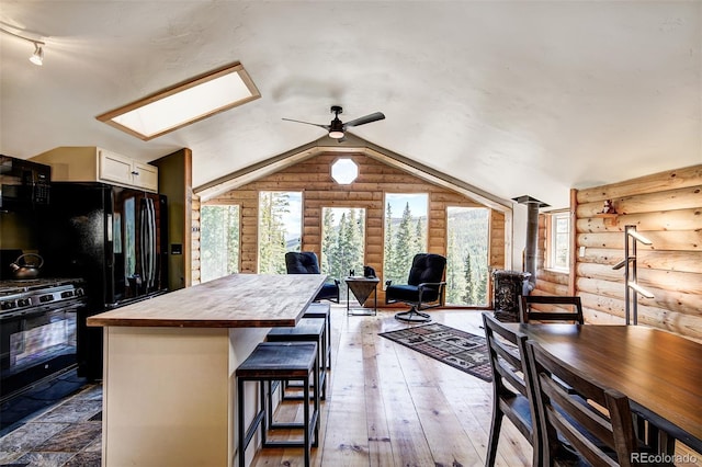 kitchen featuring wood-type flooring, a kitchen bar, black range, rustic walls, and vaulted ceiling with skylight