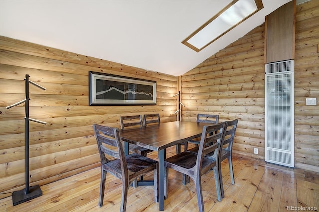 dining area featuring lofted ceiling with skylight, rustic walls, and light hardwood / wood-style floors