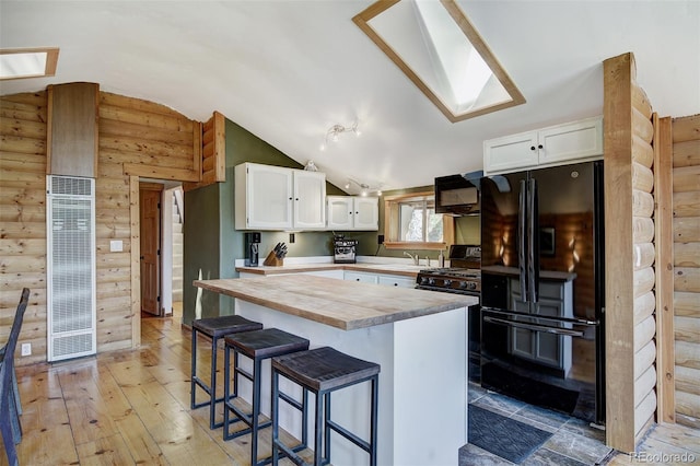 kitchen featuring vaulted ceiling with skylight, white cabinetry, black appliances, and wood-type flooring